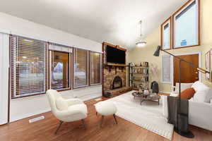 Living room with vaulted ceiling, wood finished floors, a fireplace, and healthy amount of natural light