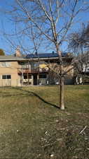 Back of house with a patio area, a lawn, a chimney, and solar panels
