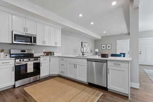 Kitchen featuring stainless steel appliances, white cabinets, a peninsula, wood tiled floors, and light stone counters