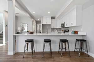 Kitchen with white cabinets, dark wood-style floors, a peninsula, range, and light stone counters