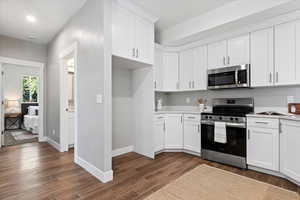 Kitchen featuring stainless steel appliances, white cabinets, dark wood-style floors, and light stone countertops