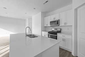 Kitchen featuring stainless steel appliances, white cabinetry, an island with sink, dark wood finished floors, and light stone counters
