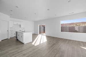Kitchen featuring white cabinets, an island with sink, open floor plan, light wood-type flooring, and plenty of natural light