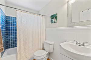 Bathroom featuring vanity, shower / bath combination with curtain, wainscoting, and a textured wall