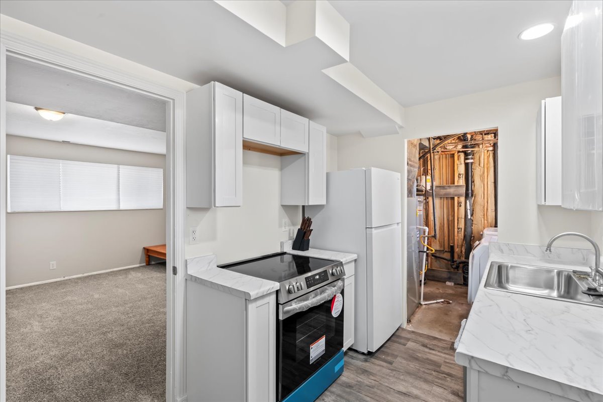 Kitchen featuring stainless steel electric range, white cabinetry, light countertops, and freestanding refrigerator