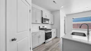 Kitchen with stainless steel appliances, light wood finished floors, a textured ceiling, light stone countertops, and recessed lighting