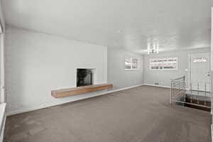 Unfurnished living room with a fireplace, carpet floors, a textured ceiling, and brick wall