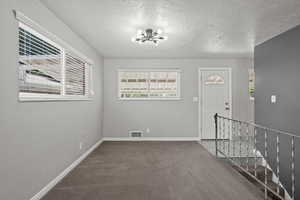 Carpeted entrance foyer featuring a chandelier and a textured ceiling