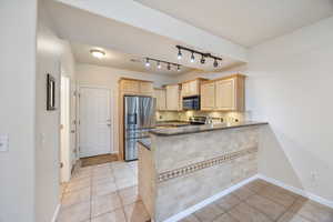 Kitchen with light wood finish cabinetry, stainless steel appliances, light tile patterned floors, tasteful backsplash, and rail lighting