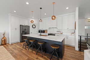 Kitchen with pendant lighting, black stainless steel appliances, a large island with sink, and tasteful backsplash