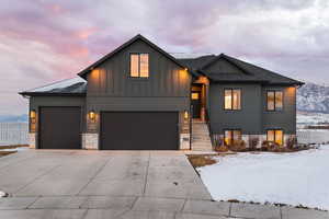 View of front facade featuring driveway, board and batten Hardie siding, a garage, and shingled roof.