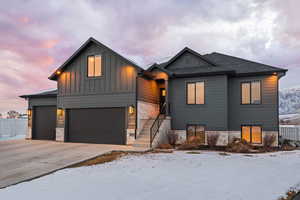 View of front facade featuring driveway, board and batten Hardie siding, a garage, and shingled roof.
