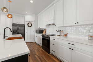 Kitchen with pendant lighting, black stainless steel appliances, a large island with sink, and tasteful backsplash