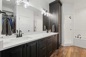 Primary bathroom featuring double sinks, dark cabinets with light quartz counters, a walk-in shower and separate soaker tub