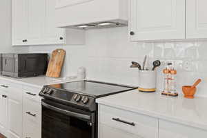 Kitchen with electric stove, white cabinetry, decorative tile backsplash, and light quartz counters.
