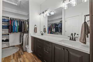 Primary bathroom featuring double sinks, dark cabinets with light quartz counters, a walk-in closet, and ensuite laundry pair.