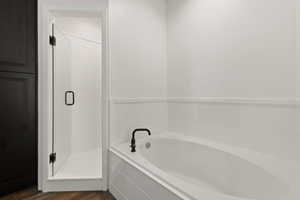 Ensuite bathroom featuring a soaker tub, a walk in shower, and dark LVP flooring