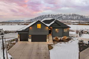 View of front facade featuring driveway, board and batten Hardie siding, a garage, and shingled roof with mountain backdrop.