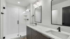 Photos are of a completed unit - Bathroom featuring double vanity, a stall shower, recessed lighting, and light wood finished floors