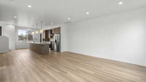 Photos are of a completed unit - Kitchen featuring open floor plan, a center island with sink, stainless steel appliances, light wood-style floors, and decorative light fixtures