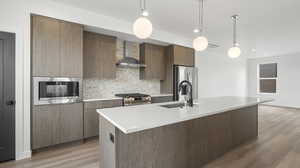 Photos are of a completed unit - Kitchen featuring modern cabinets, backsplash, pendant lighting, a kitchen island with sink, and stainless steel appliances