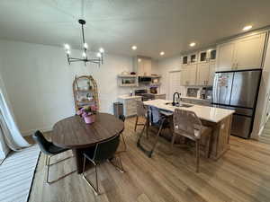 Kitchen with stainless steel appliances, a textured ceiling, a kitchen island with sink, hanging lights, and a kitchen breakfast bar