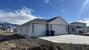View of front of house with a garage, stone siding, driveway, roof with shingles, and a mountain view
