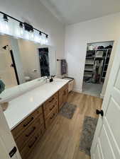 Full bath featuring a spacious closet, vanity, light wood-style flooring, and a shower