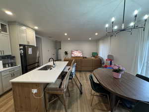 Dual tone kitchen featuring open floor plan, a kitchen bar, a center island with sink, freestanding refrigerator, and light wood finished floors