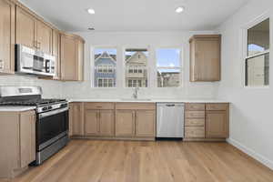 Kitchen featuring stainless steel appliances, light wood-style floors, recessed lighting, backsplash, and light stone countertops
