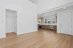Unfurnished living room featuring recessed lighting, light wood-type flooring, and a high ceiling