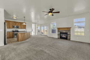 Kitchen with open floor plan, light colored carpet, stainless steel appliances, a ceiling fan, and a stone fireplace