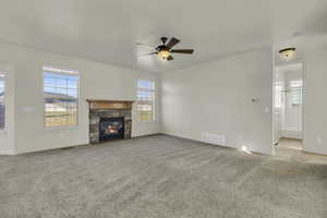 Unfurnished living room featuring ceiling fan, carpet flooring, a fireplace, and crown molding