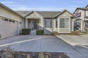 View of front of home with stucco siding, stone siding, roof with shingles, driveway, and a garage