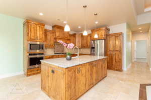 Kitchen with wood finish cabinets, stainless steel appliances, light stone countertops, and stone tile floors