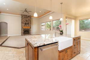 Kitchen featuring stone tile flooring, wood finish cabinetry, stainless steel dishwasher, pendant lighting, and a center island with sink