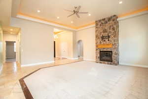 Unfurnished living room with a fireplace, ceiling fan, a raised ceiling, arched walkways, and inlaid floor details
