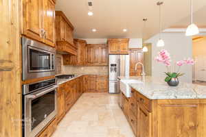 Kitchen featuring wood finish cabinetry, stone tile flooring, stainless steel appliances, and light stone countertops