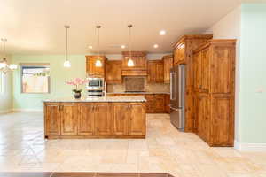 Kitchen featuring wood finish cabinetry, light stone counters, a center island with sink, stainless steel appliances, and stone tile flooring