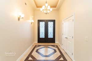 Entryway featuring inlaid floor details, hanging lights, a raised ceiling, and french doors