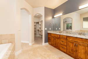 Bathroom featuring double vanity, stone tile floors, a bath, a spacious closet, and a ceiling fan