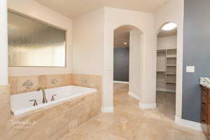 Full bath featuring vanity, a walk in closet, a bath, and stone tile flooring