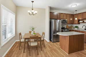 Kitchen with stainless steel appliances, suspended lighting, light wood-type flooring, a center island, and wood finish cabinets