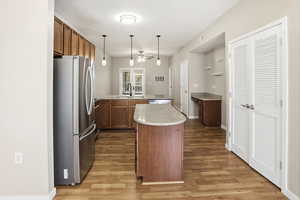 Kitchen featuring freestanding refrigerator, decorative light fixtures, light wood finished floors, wood finish cabinetry, and light stone counters