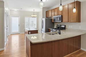 Kitchen featuring stainless steel appliances, a center island, a peninsula, wood finish cabinets, and light stone countertops