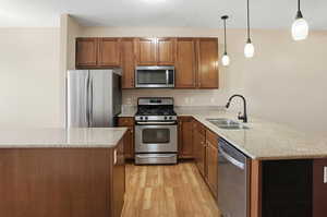 Kitchen featuring stainless steel appliances, light stone counters, light wood-type flooring, and wood finish cabinets
