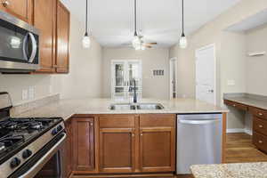 Kitchen featuring stainless steel appliances, light stone counters, a peninsula, hanging light fixtures, and dark wood-style flooring
