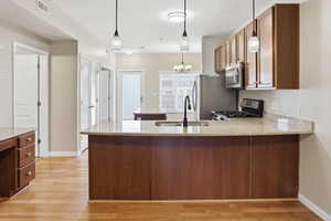Kitchen featuring light stone counters, a peninsula, stainless steel appliances, hanging lights, and light wood-type flooring