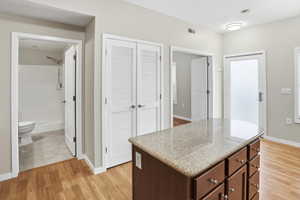 Kitchen with light wood finished floors, a kitchen island, light stone countertops, and dark wood finish cabinetry