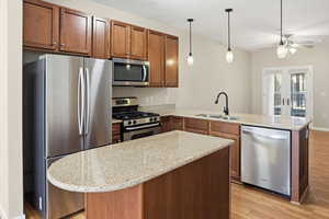 Kitchen featuring stainless steel appliances, a peninsula, light wood-type flooring, light stone countertops, and pendant lighting